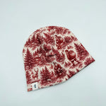 Newbornlander Christmas Scene beanie hat for babies, red toile print with Santa, deer and winter cabin on cream cotton, side view