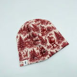 Newbornlander Christmas Scene beanie hat for babies, red toile print with Santa, deer and winter cabin on cream cotton, side view